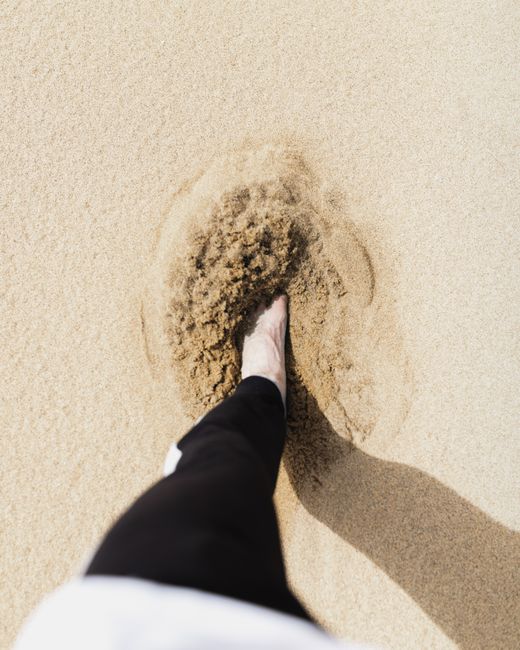 Close-up of a bare foot stepping into golden sand in Sardinia, Italy.