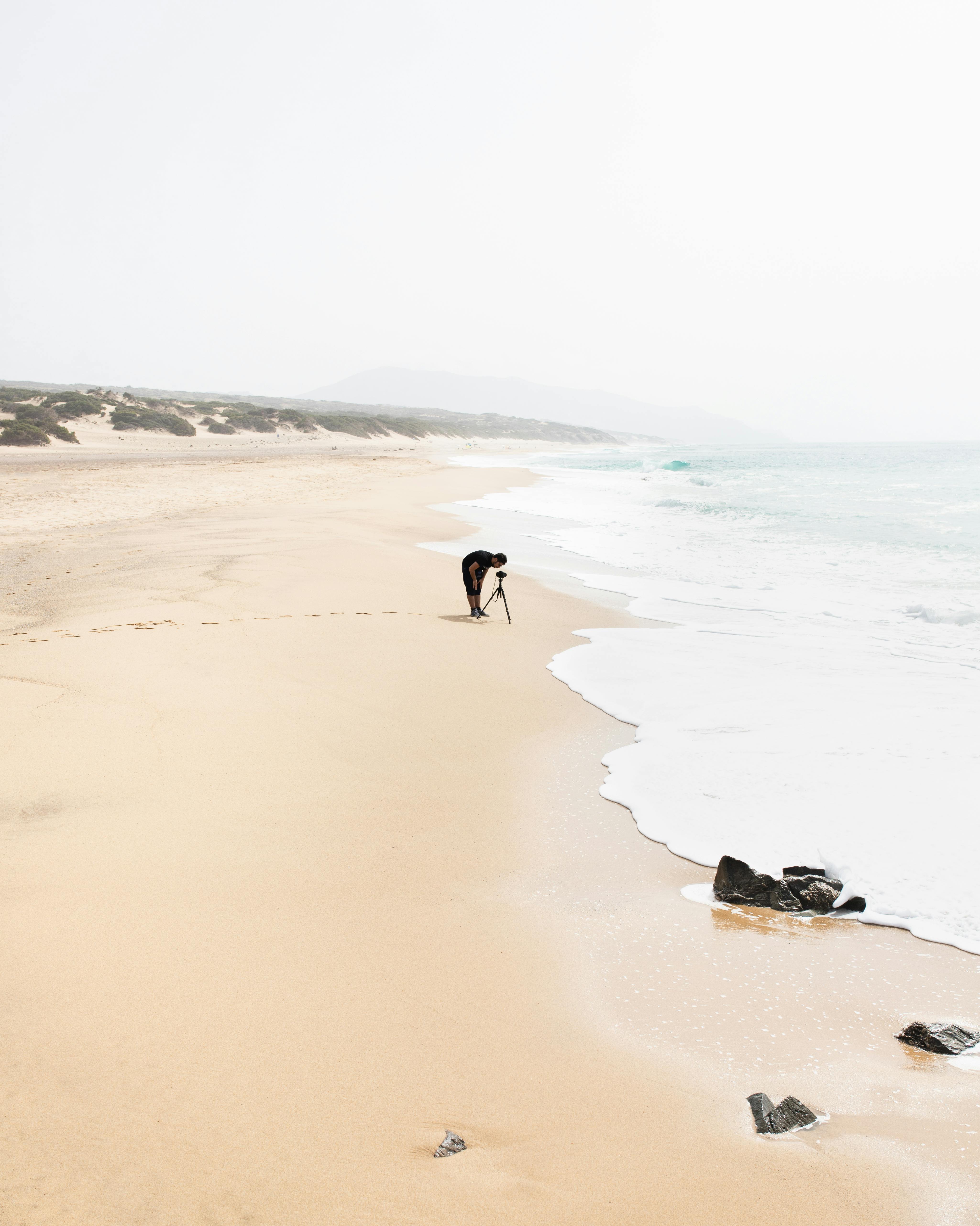 A lone photographer captures waves on a misty Sardinian beach.