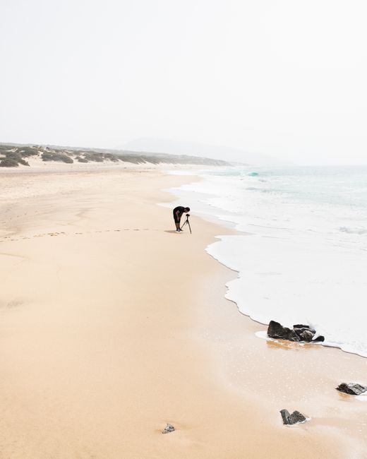A lone photographer captures waves on a misty Sardinian beach.