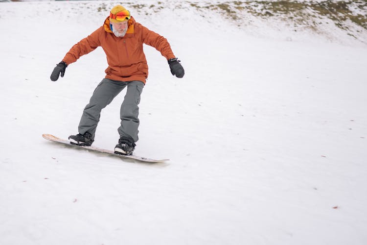 An Elderly Man Snowboarding In The Snow