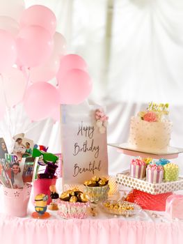 Charming dessert table setup for a birthday with pink balloons, cake, and treats.
