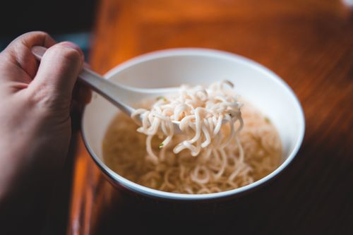 Free A hand holding a spoonful of instant noodles over a bowl, perfect for food-related designs. Stock Photo