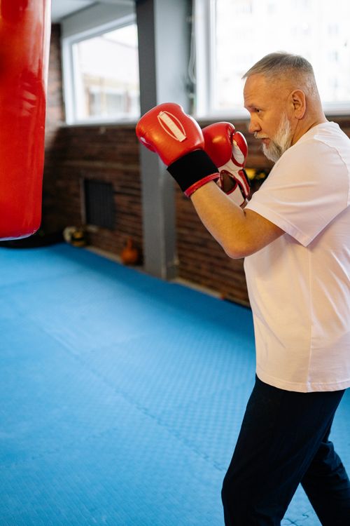 Free Elderly man practicing boxing indoors with red gloves, focusing on fitness. Stock Photo