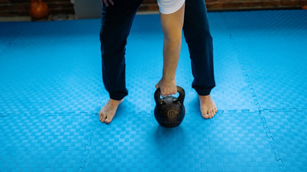 An adult man lifting a kettlebell on blue rubber mats indoors, emphasizing fitness and strength.