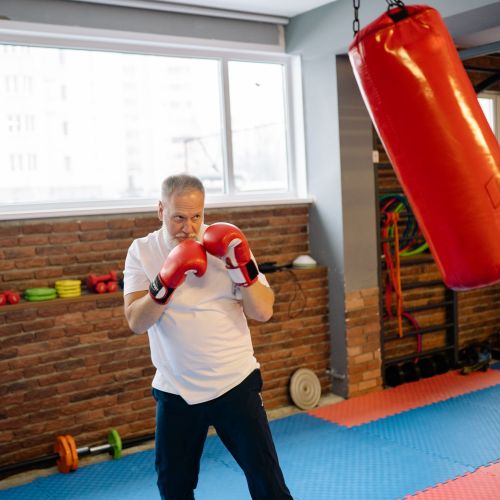 Free Elderly man practicing boxing indoors with red gloves and heavy bag. Stock Photo