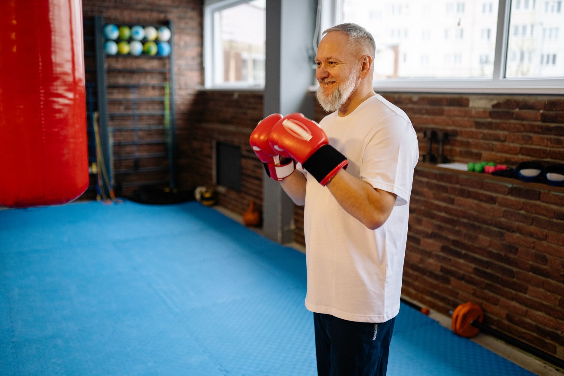 ivermectin for long covid fatigue older adults — Elderly man with gray hair exercising with boxing gloves in a gym setting for fitness.