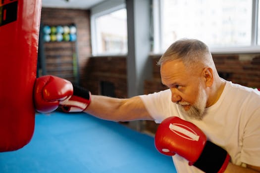 Elderly man punching boxing bag indoors, promoting fitness and health.