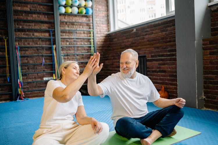 An Elderly Couple High Fiving Each Other While Sitting In The Gym