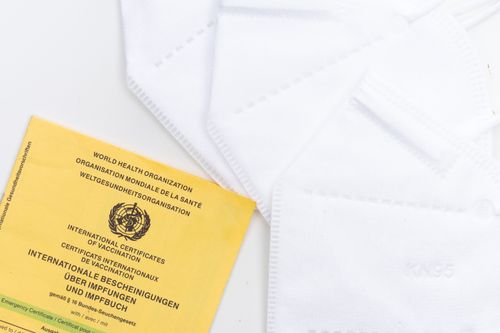 Free A WHO vaccination card alongside KN95 masks on a white surface, symbolizing health protection and safety. Stock Photo