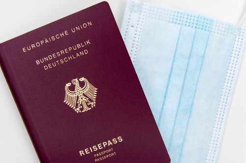 Free Top view of a German passport next to a surgical mask, symbolizing travel during pandemic. Stock Photo