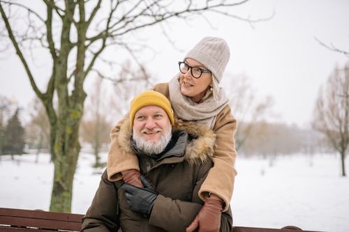 Free Elderly couple in winter clothes smiling while outdoors in a snowy park. Stock Photo