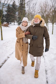 Elderly couple in winter clothes walking happily outdoors in a snowy park.