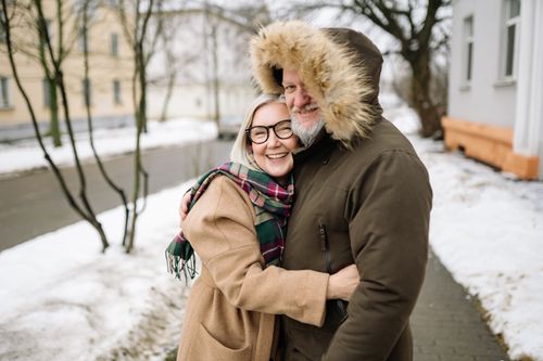 Free Happy senior couple in winter coats smiling and embracing outdoors on a snowy day. Stock Photo