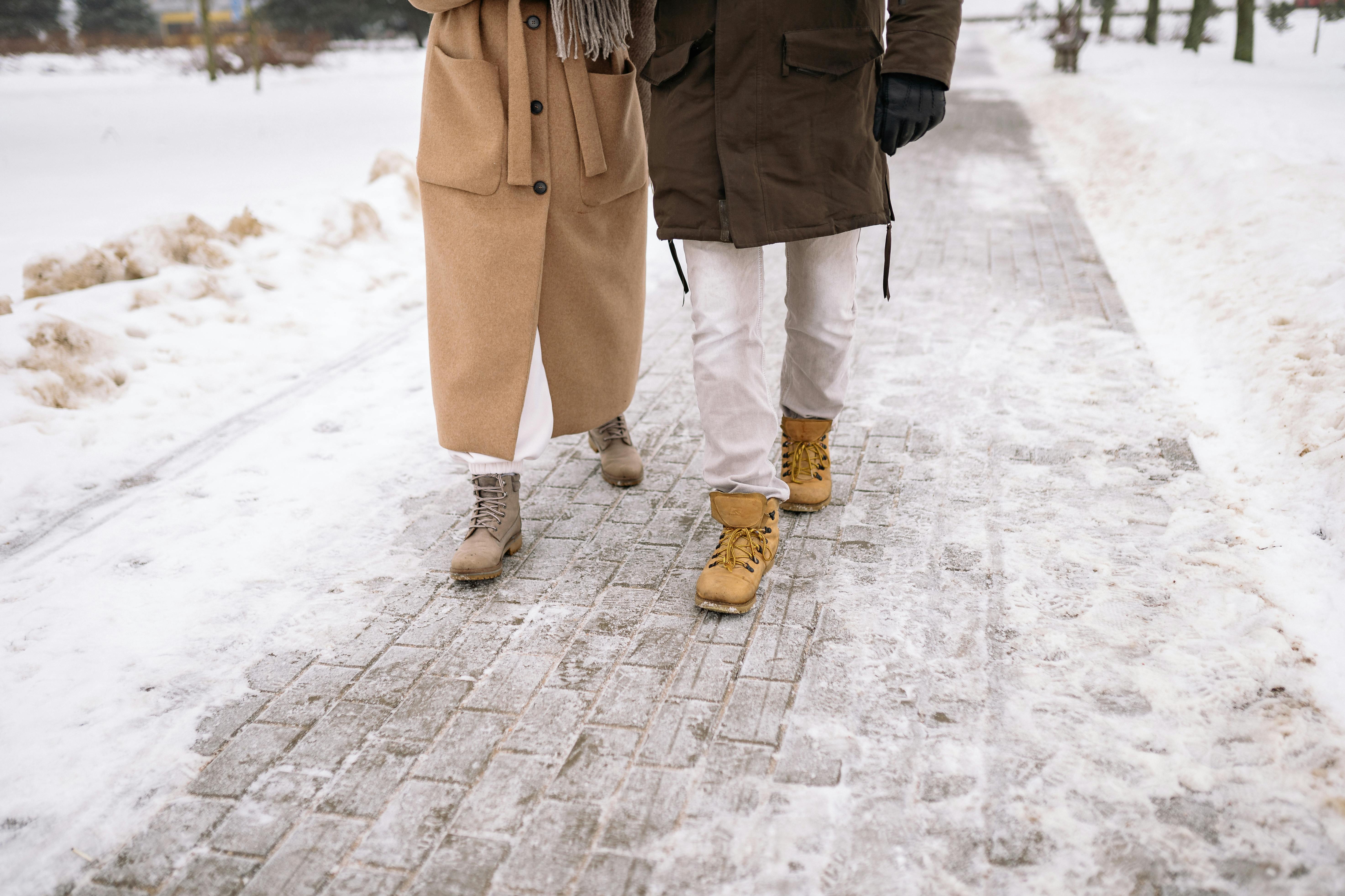 Person in Brown Coat and White Pants Standing on Snow Covered Ground