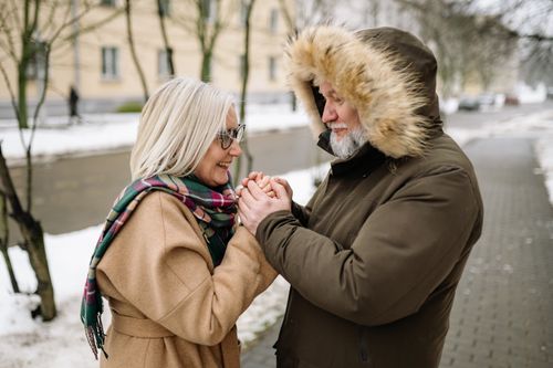 Free Senior couple enjoying a winter day, holding hands warmly on a snowy sidewalk. Stock Photo