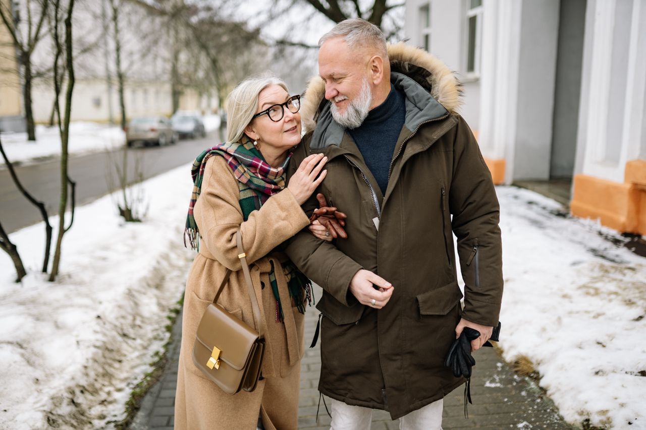 Happy senior couple in winter coats walking on a snowy street