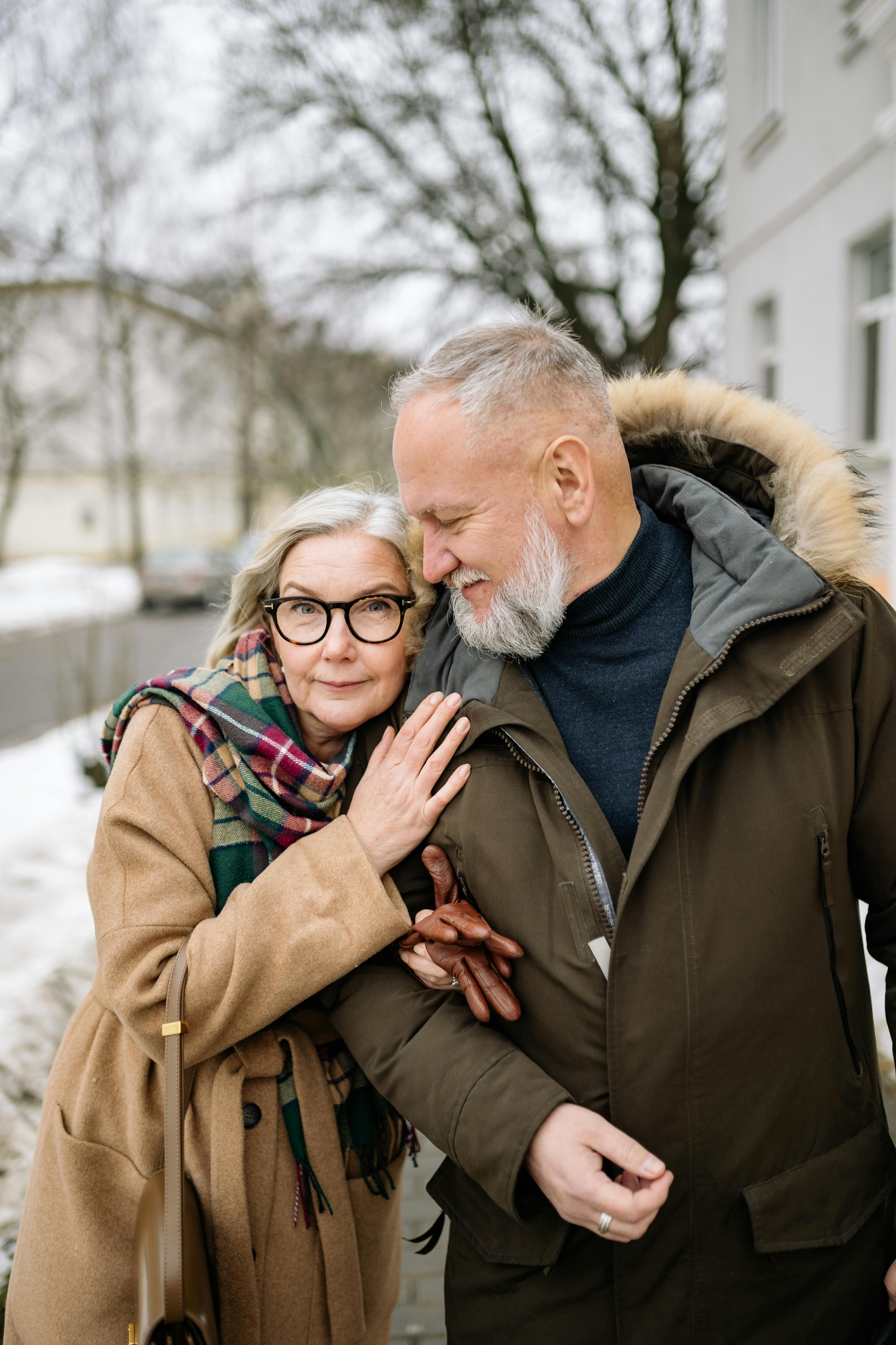 A loving senior couple in winter clothes, walking and embracing outdoors in a snowy setting.