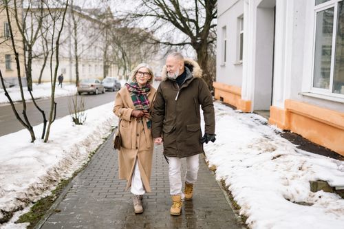 Free Elderly couple walking hand in hand on an urban snowy sidewalk, showcasing love and connection. Stock Photo