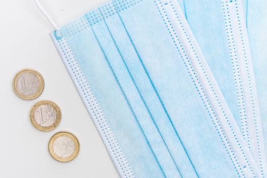 Flatlay of surgical face masks and euro coins, symbolizing pandemic economic challenges.