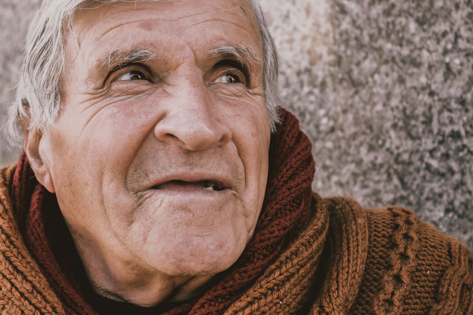 A close-up portrait of a thoughtful senior man wearing a cozy sweater, looking into the distance.