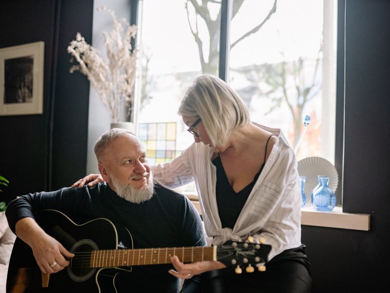 An older couple at home, the man playing an acoustic guitar.