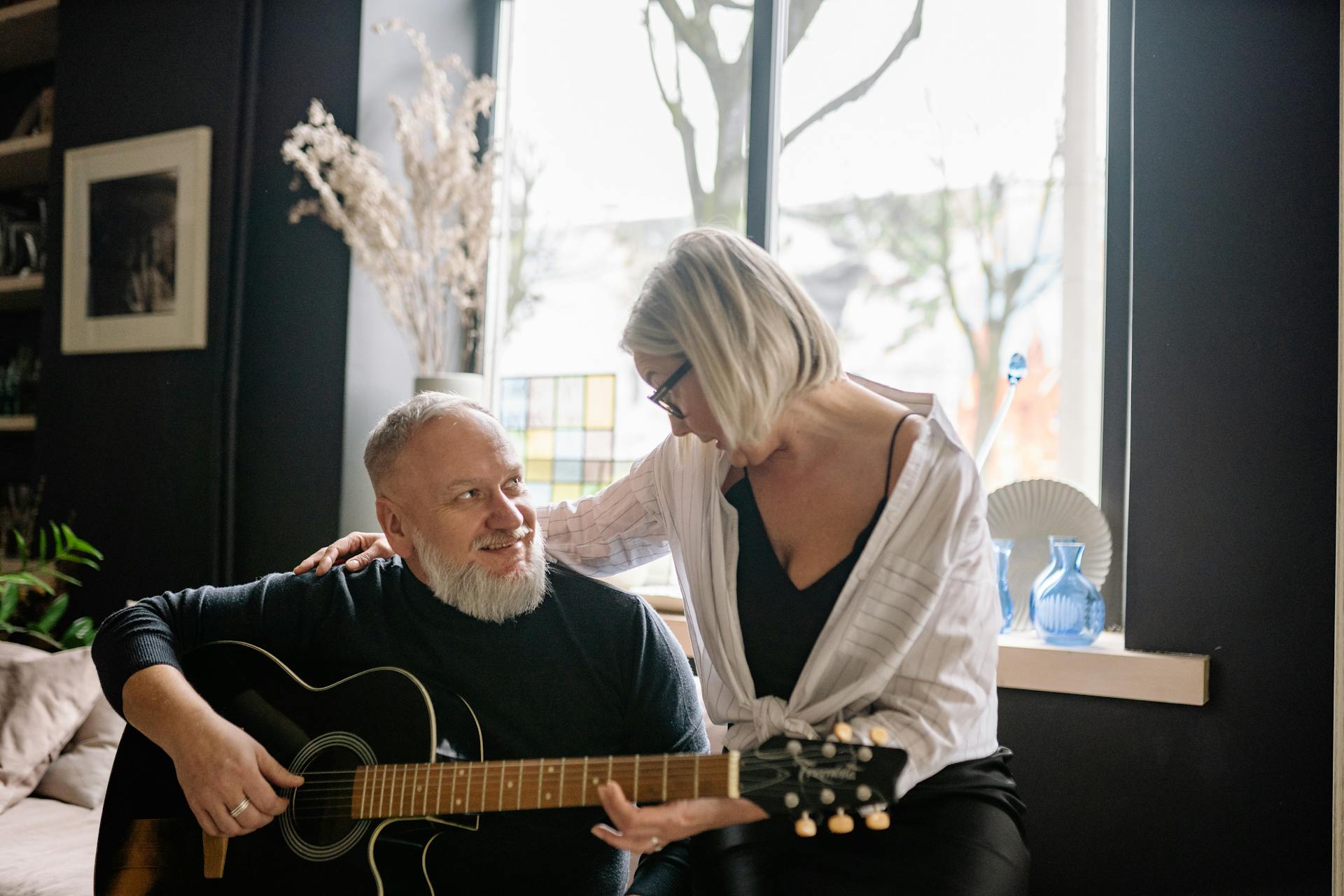 Elderly couple relaxing at home as the man plays an acoustic guitar, radiating warmth and joy.