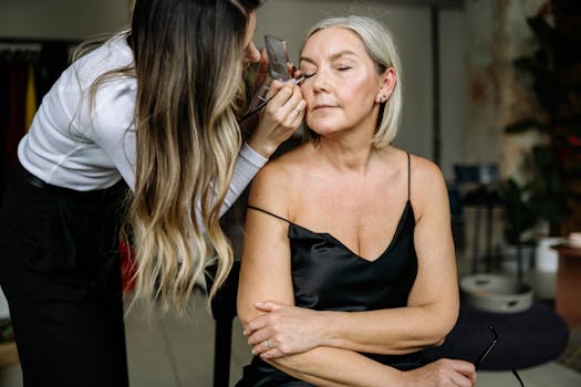 A makeup artist skillfully applies eye makeup to a senior woman, enhancing her features.