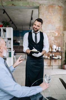 A smiling waiter taking an order from a customer in a trendy café setting.