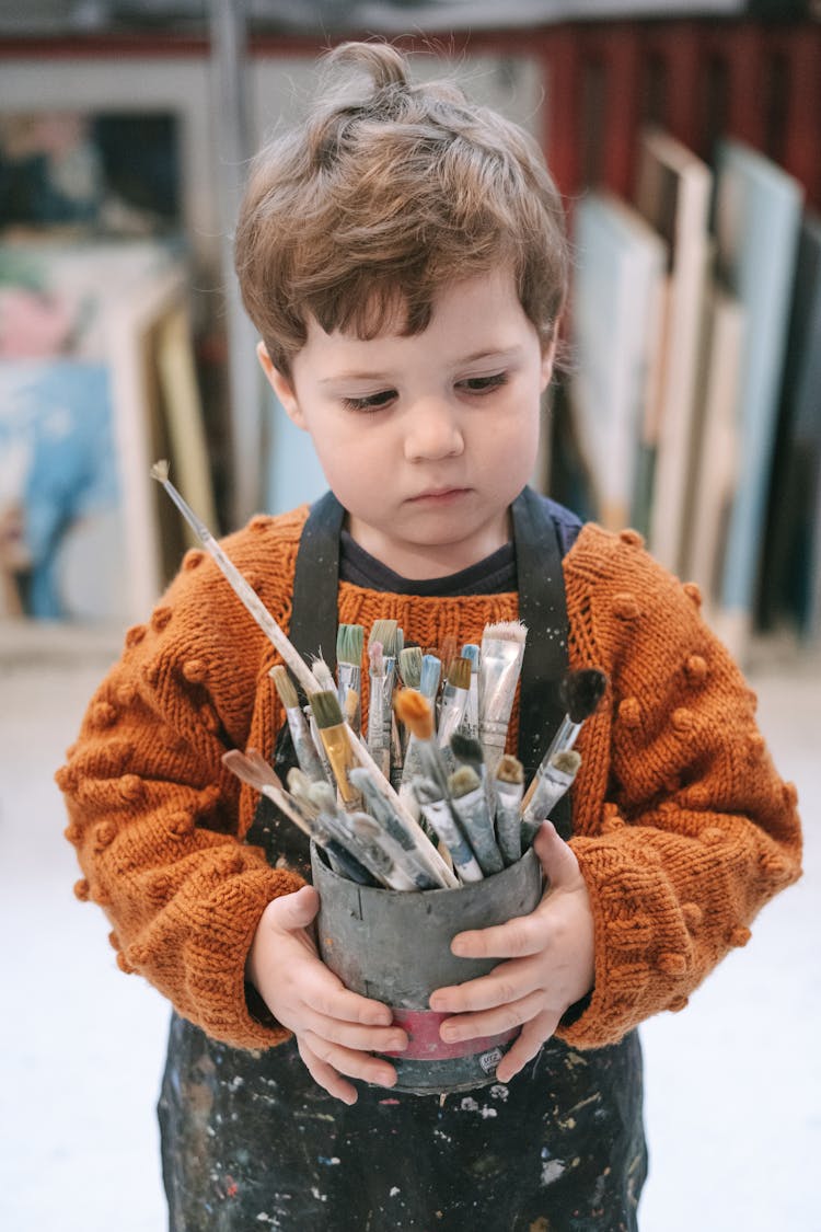 A Cute Little Boy Holding A Holder With Paintbrushes