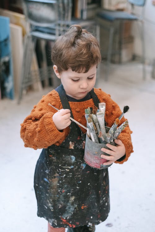 A Boy Holding a Container of Paintbrushes