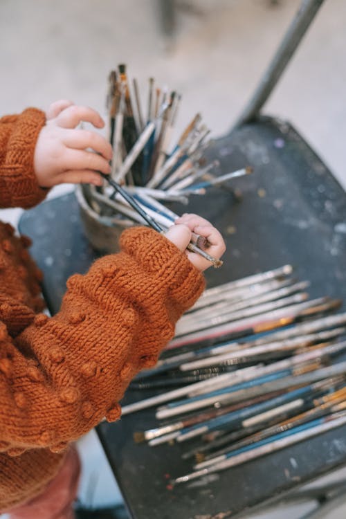 A Kid Orange Knit Sweater Holding a Paint Brush