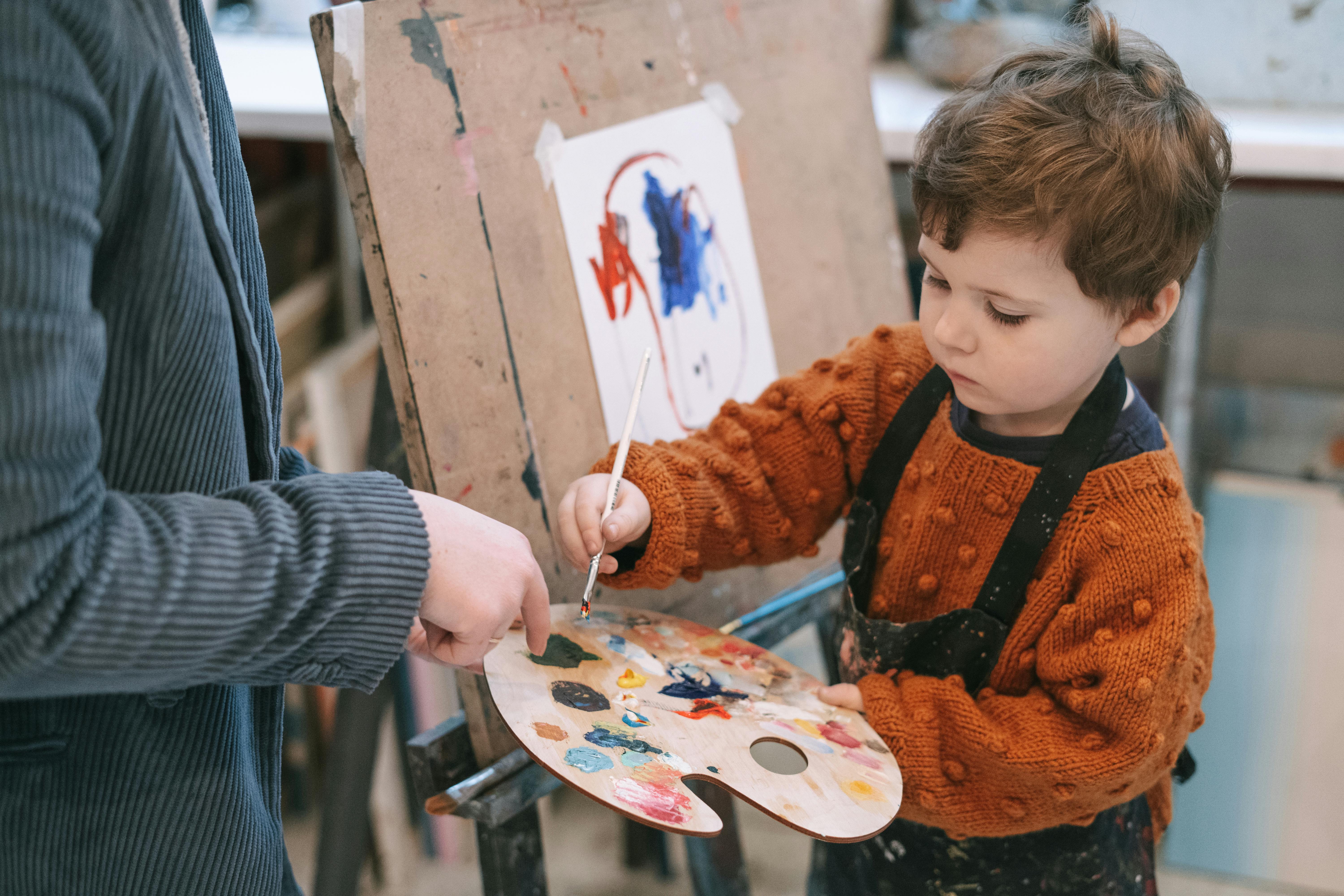 boy in orange and black zip up jacket holding white and red floral round plate