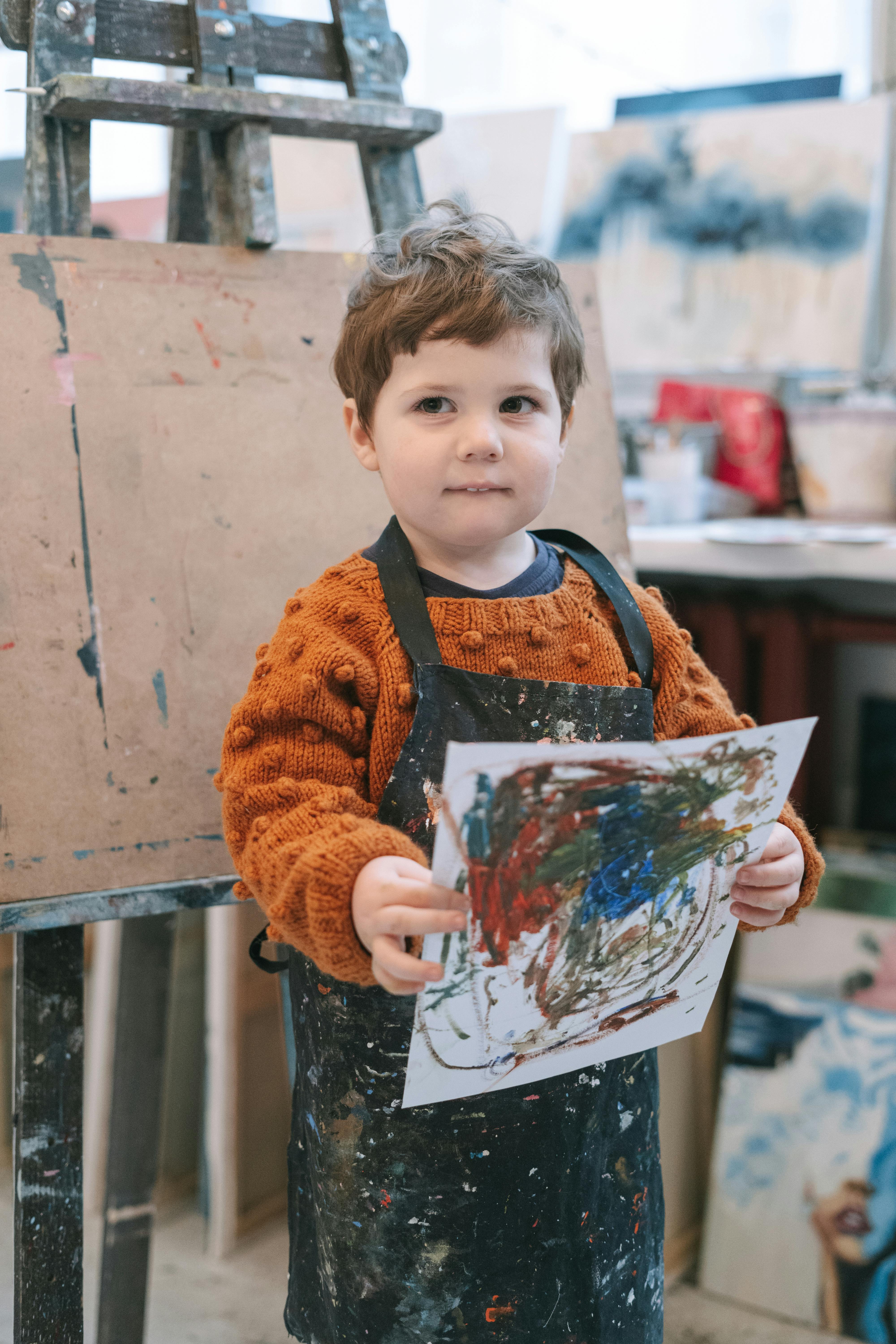 boy in orange and brown sweater holding white and blue floral painting