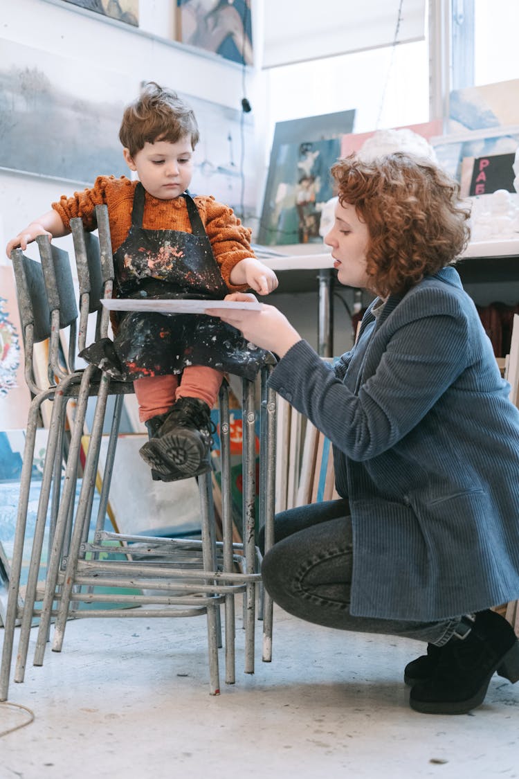 A Kid In Orange Sweater Sitting On The Stacks Of Chairs 