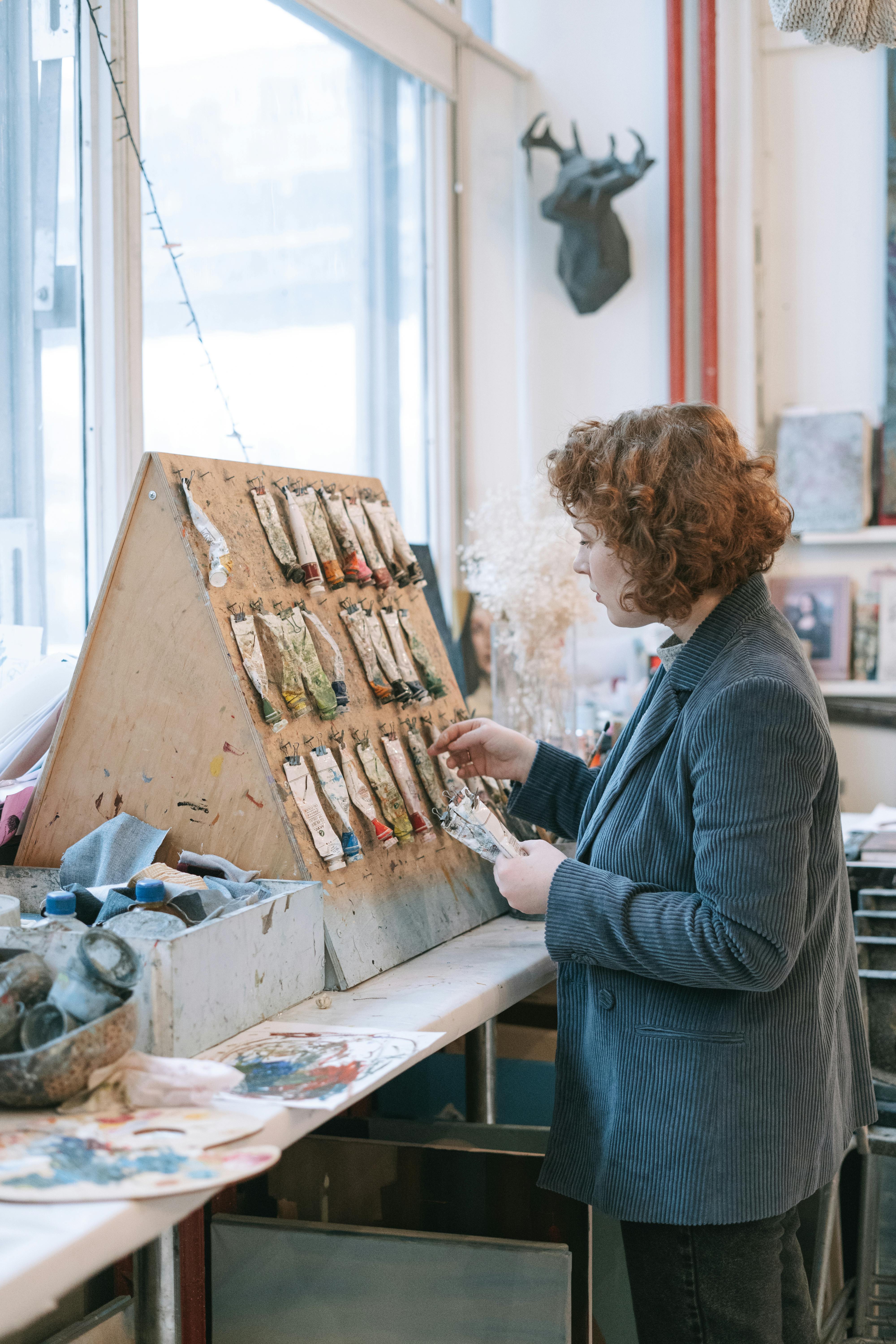 a woman wearing blazer hanging the tubes of acrylic paint on the board