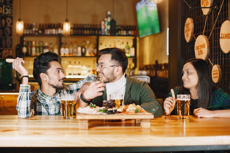 Men And Woman Drinking Beer And Eating Snacks In A Bar