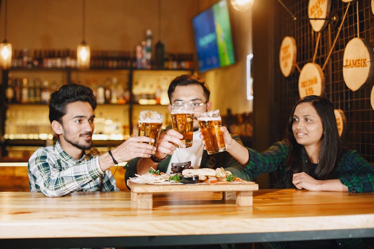 Men And Woman Making A Toast With Beer Glasses At A Bar Table