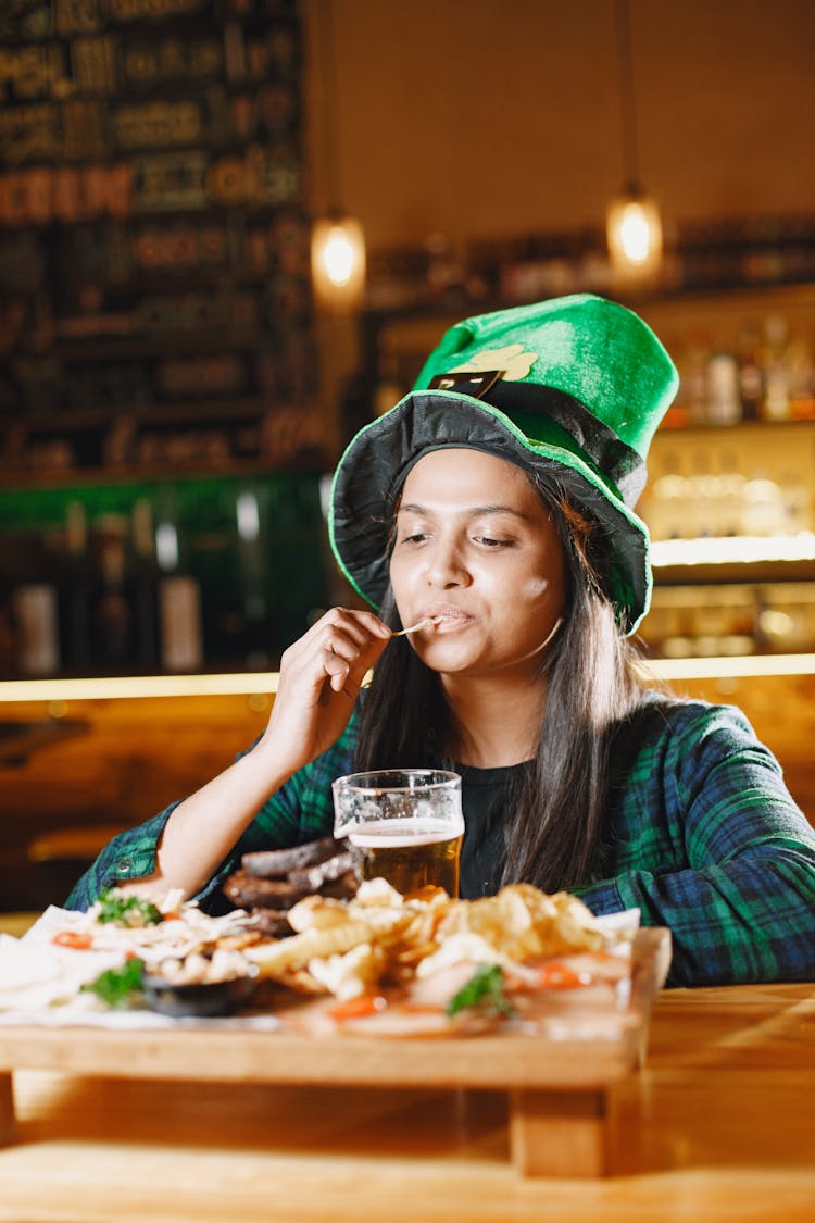 Woman In A Green Hat Eating Snacks And Drinking Beer In A Bar