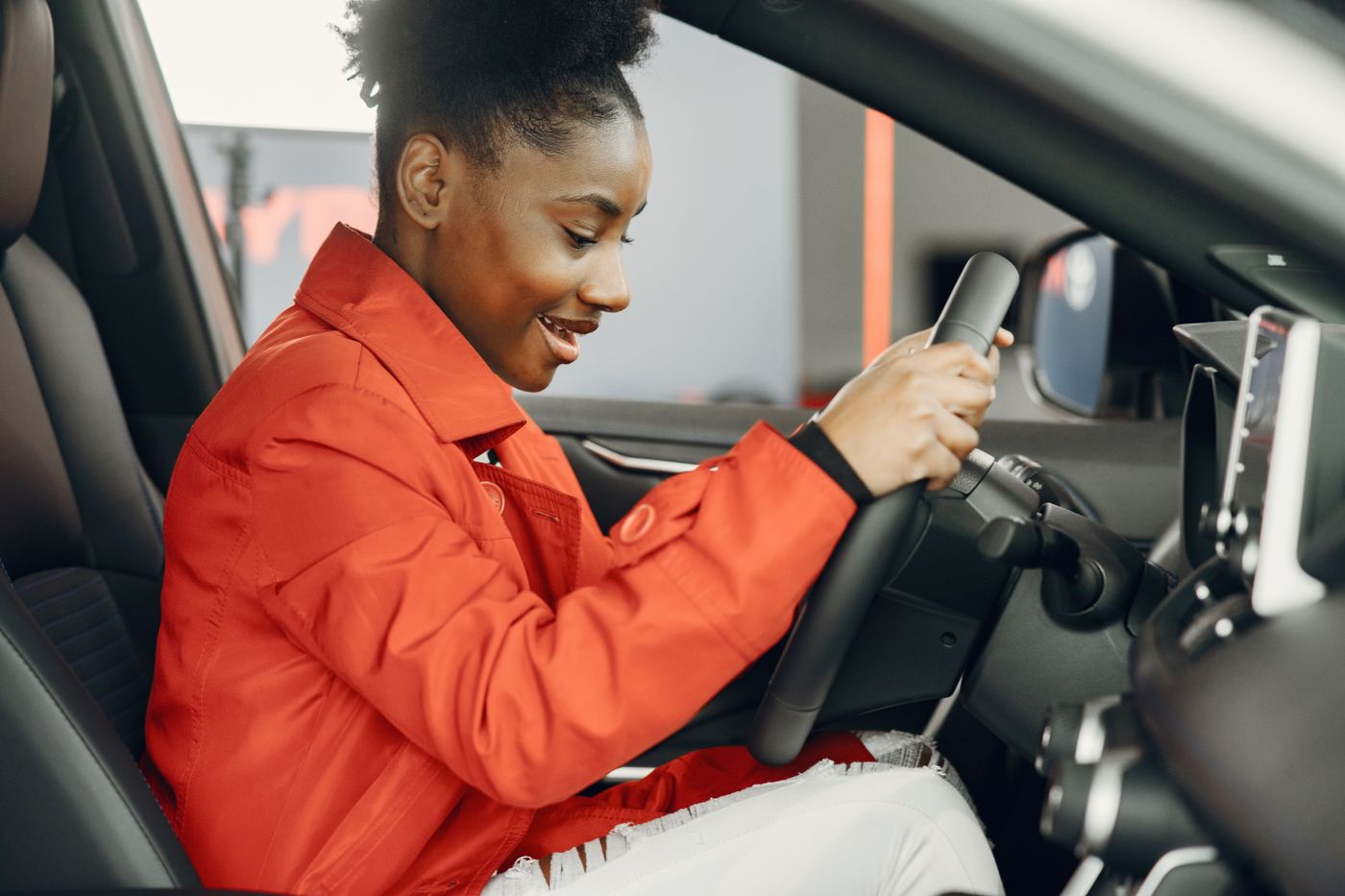 Jeune femme essayant le volant d'une voiture, assise côté conducteur