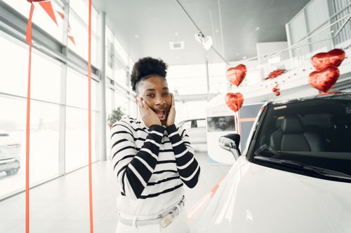 Free A woman with short hair is surprised by a new car gift decorated with heart-shaped balloons indoors. Stock Photo