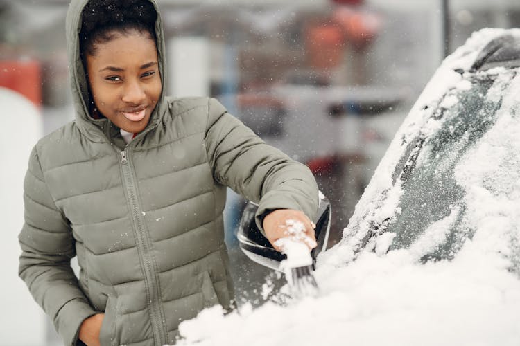 Portrait Of A Young Woman Brushing Snow Off A Car