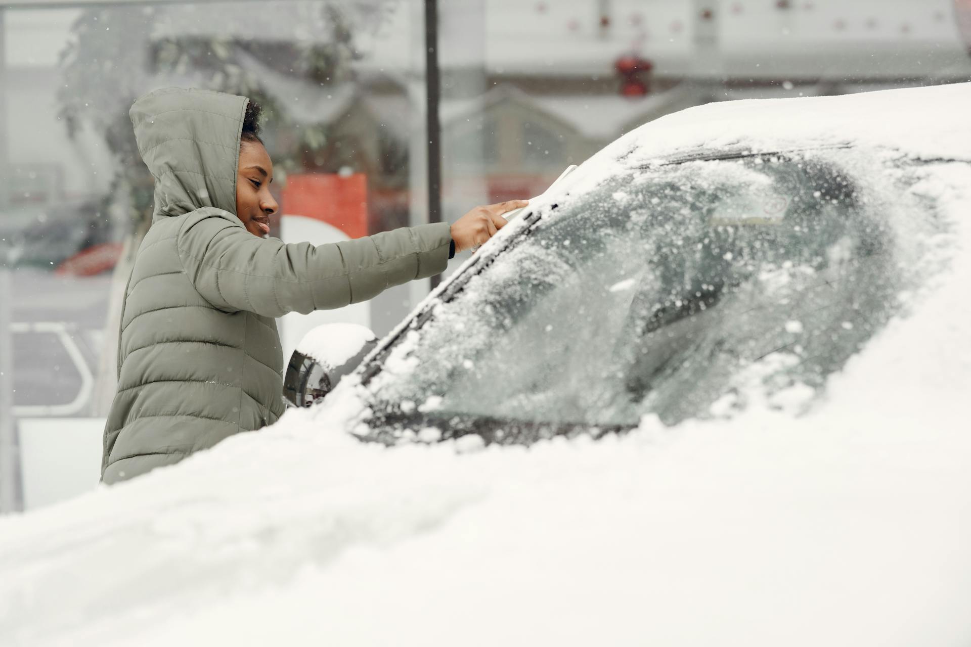 African American woman removing snow from car during a winter day outdoors.