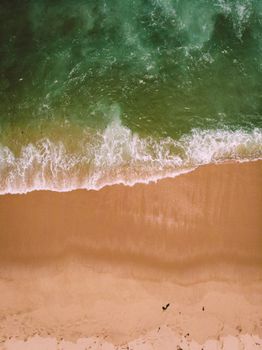 Aerial top view of green waves crashing on a sandy beach in Brazil. Perfect for travel and nature themes.