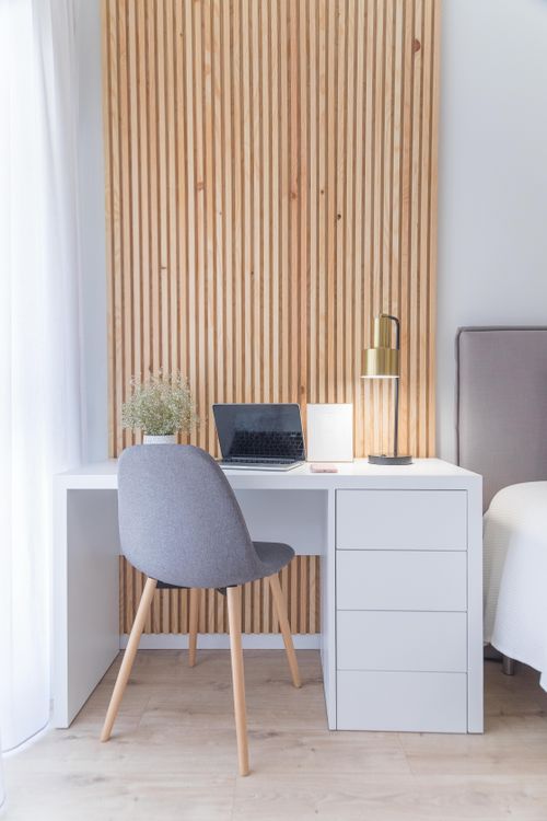 Free Stylish minimalist workspace featuring a laptop, lamp, and white desk against a wooden panel backdrop. Stock Photo