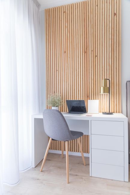Photo by SANDRA REI on Pexels Clean and cozy workspace featuring a gray chair, white desk, and a laptop set against a warm wooden panel.
