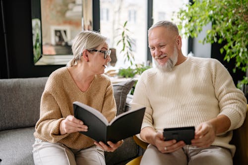 Free Elderly Couple Reading a Book while Sitting on the Sofa Stock Photo