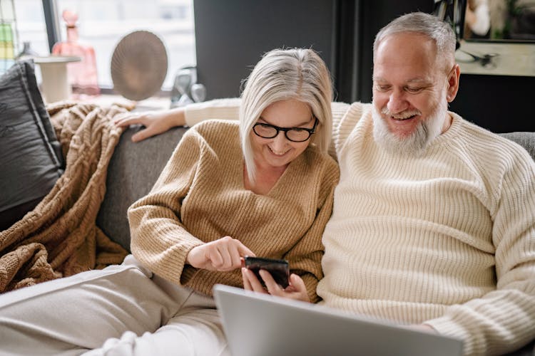 Elderly Couple Sitting On Sofa Using Phone 