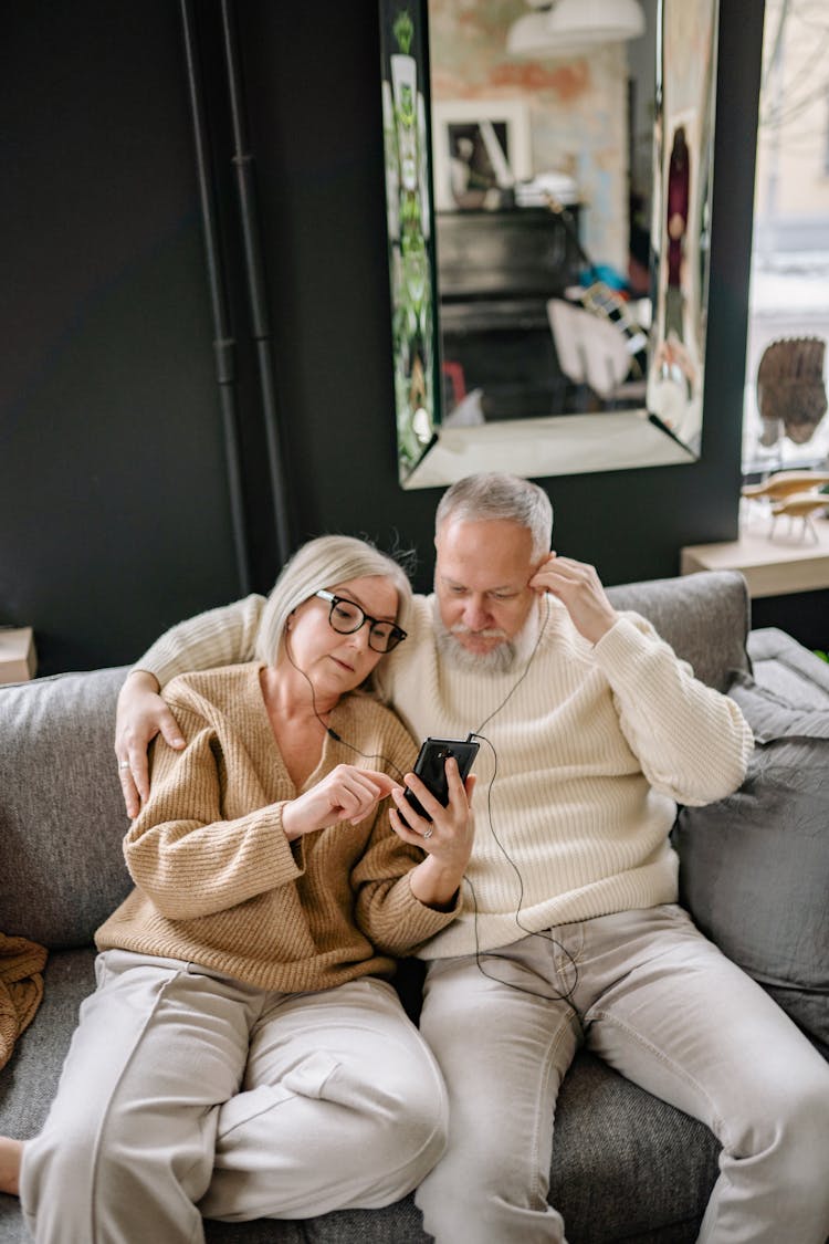 An Elderly Couple Sitting On A Couch While Listening To Music