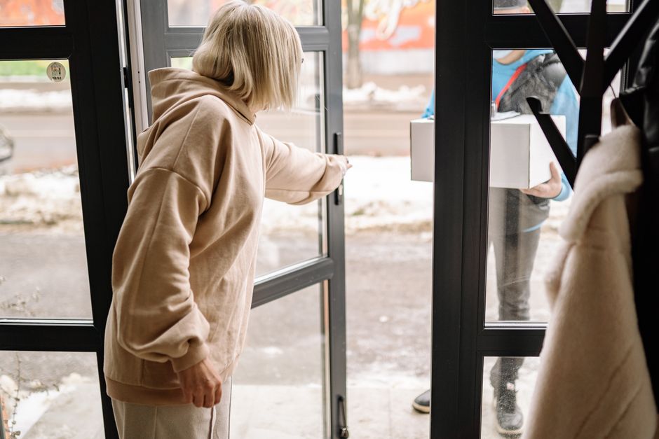A calm, neutral school pickup point with two adults exchanging a small backpack; clear light, neutral colors. Captured by Yan Krukau