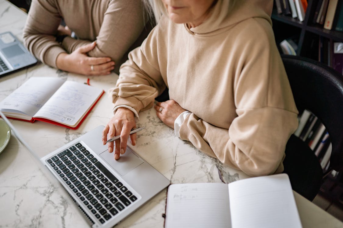 Free Woman in Brown Hoodie Sitting Beside Table With Macbook Pro Stock Photo